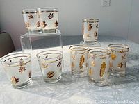 Two sets of vintage frosted Libbey glasses arranged on a table showing gold leaf pattern on frosted glass surface
