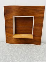 Front view of the Umbra hanging wall display showing curved wood veneer panel with central display area and light wooden shelf