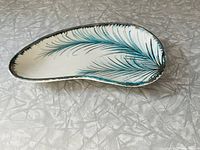 Full view of the ceramic dish showing its elongated curved shape and botanical frond design in turquoise and silver.