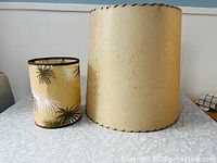 Pair of vintage lampshades sitting side by side on a white patterned surface, showing size difference and general condition.