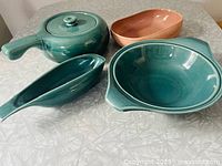 Photo showing all four pieces: seafoam green covered casserole with handle, coral serving dish, seafoam green serving dish, and seafoam green gravy boat on tabletop.
