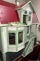 View showing front exterior with red roof, cream siding, green trim, bay window and open functional door.