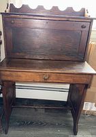 Front view of antique oak child-sized desk showing drop-front door in closed position with scalloped top back panel