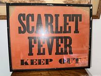 Front view of framed Scarlet Fever quarantine sign, orange background with black text saying 'SCARLET FEVER KEEP OUT'.