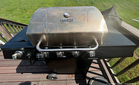 Front side view of grill with lid closed showing Char-Broil branding on lid and four stainless steel control knobs.