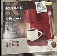 Photo of the original box showing the Keurig K-Express Essentials red coffee maker with branding, key features like 3 cup sizes, 10 oz max, and recyclable K-Cup pods.