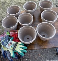 Seven small terra cotta planters with drainage holes and matching saucers, accompanied by four pairs of new outdoor gardening gloves in green, blue, and red colors.