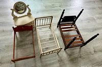 Wooden antique doll furniture set including three beds and one dresser with mirror, laid out on a light wood floor.