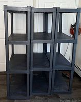 Front view showing three black plastic shelving units stacked with three shelves each, exhibiting wear marks and usage residue.
