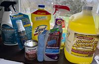 Cleaning supplies grouped on a surface showing various bottles and cans, some with spray nozzles, brands include Lysol, Rejuvenate, Rust-Oleum.