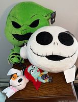 Front view of the lot showing Oogie Boogie and Jack Skellington large pillows and four small plush clips placed on a table.