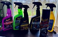 Six car care products on a windowsill, including five Meguiar's spray bottles and one aerosol can plus one RainX spray bottle.