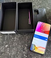 Smartphone with case, box, and purple stylus displayed on counter.