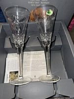 Pair of crystal champagne flutes displayed upright in original box with informational inserts visible.