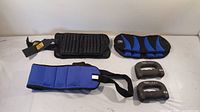 Full view of all items laid out including two pairs of ankle weights, hand weights, and blue weighted belt.