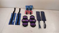 Photo showing five pairs of wrist and ankle weights in blue, pink, purple, and black colors, arranged on a plain surface