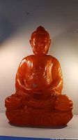 Front view of a large orange translucent resin Buddha statue with detailed robes and serene expression, showing overall condition and chip on forehead.