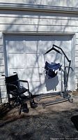Full view of patient hoist and wheelchair positioned outdoors against garage door.