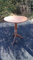 Full view of the round pine wood tilt top table outdoors, showing the flat horizontal table surface and the three-legged pedestal base.