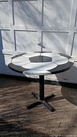 Round table with painted wood tabletop featuring a soccer ball pattern, shown in sunlight in front of a white garage door.