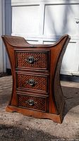 Front view showing three drawers with woven wood fronts and metal ring handles, and curved side profile.