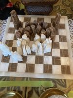 Full view of the onyx chessboard with all chess pieces set up on the board. The board has squares alternating in brown and white onyx. The chess pieces are carved with distinctive geometric shapes, with the two colors white and brown clearly visible.