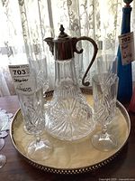 Front view of glass decanter with silver top flanked by crystal flutes on round silver tray