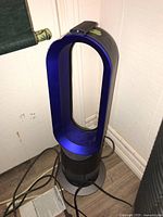 Front view of Dyson AM05 bladeless fan heater showing silver and blue oval loop design on wooden floor.