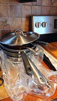 Stack of frying pans with handles, one with glass lid on top