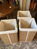 Three faux wicker hampers shown together on carpeted floor with white fabric liners inside.