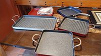 Overview of three grill pans with handles, two have ridged surfaces, one smooth surface, with a baking pan with rack placed on top