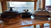 Wide shot showing three pottery dishes with lids on a shelf by a window with natural light. The largest dish is on the left, medium center, smaller right.