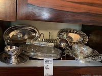 Wide shelf view depicting various silver plated serving pieces including trays, toaster rack, gravy boat, and covered bowl.