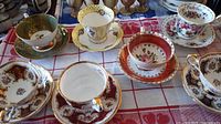 Six vintage teacups and saucers with floral and decorative patterns, varying styles and colors observed on a cloth.