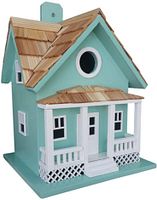 Birdhouse shaped like a green and white cottage with wooden shingles on roof and porch