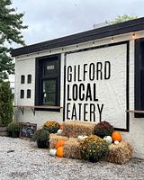 Exterior photo showing the Gilford Local Eatery sign on a wall decorated with pumpkins and hay bales.