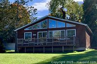 Exterior of wood-sided waterfront cottage with large picture windows and elevated deck overlooking yard