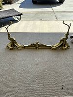 Front view of the brass fireplace fender showcasing its ornate curved design and adjustable middle section.