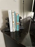 Pair of decorative metal bookends holding five books, showing their size and look on a dark surface