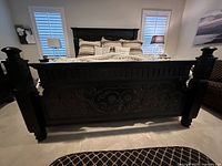 Front view of ornate black wood king bed frame showing carved floral and scroll details on footboard and headboard