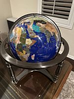 Front-right angled view showing the blue ocean and colorful stone continents with labeled countries on the globe with metal stand underneath.