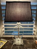Full view of lamp front on against window blinds, showing black rectangular fabric shade and clear crystal base.