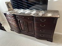 Front view of dark brown Thomasville dresser with polished marble top and metal handles, TV on top.