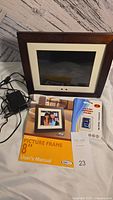 Photo showing wood-framed 8-inch digital picture frame, remote control, power adapter, user manual, and new 16GB memory card in blister package.