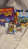 Lot showing Top Secret Spy activity kit, Marvel Chess box, Monopoly Deal card game, and Voice Over Robot toy in packaging.