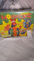 Photo of the sealed box front showing colorful gears and monster design. The box states 'Motorized Monsters' with 'real sound', 69 pieces, age 6+.
