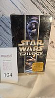Front view of sealed Star Wars Trilogy VHS box set with gold logo, spaceship art, and promotional sticker.