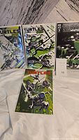 All four Teenage Mutant Ninja Turtles comic books arranged with three standing and one laid flat, showing cover art in black, white, green color palette mostly from the Black White & Green series.