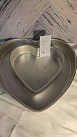 Large and small silver metal heart-shaped baking molds shown nested together on a white cloth background