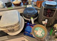 Wide view of the lot showing the Ninja air fryer, T-fal fryer, roasting pan with lid, paper and silicone liners, and turkey platter underneath.